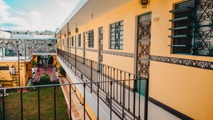 Um edifício amarelo com janelas numeradas, uma varanda com grades de metal e um pátio com plantas em vasos.
