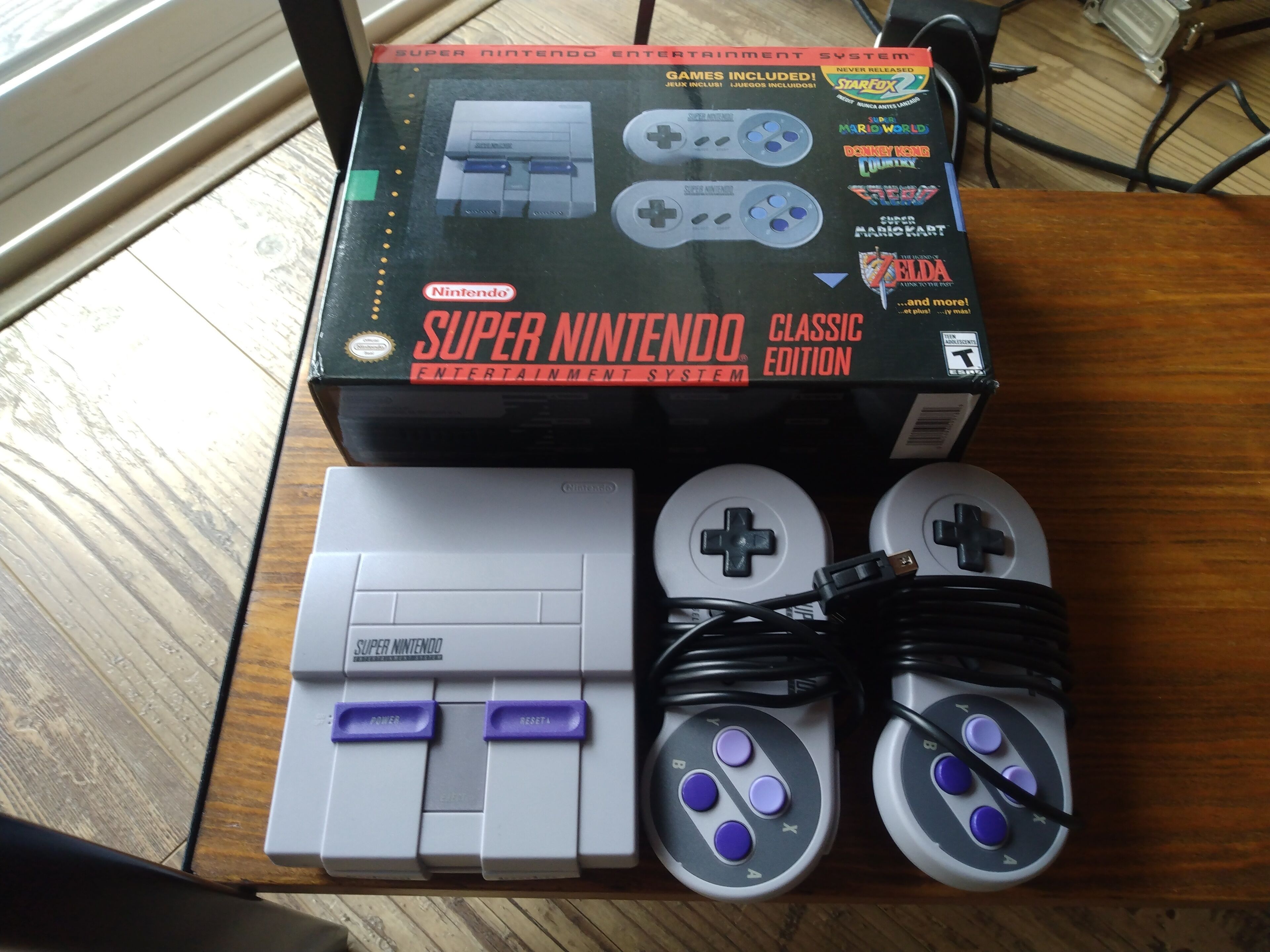 Eine Super Nintendo Entertainment System-Verpackung, Konsole, Controller und Zubehörteile auf einer Holztisch.