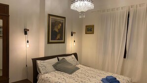 Een slaapkamer met een bed, een kroonluchter, twee wandlampen, een schilderij en een raam met gordijnen.