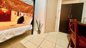 A room with a bed, a small potted plant, a door, and a desk with a chair. - Apartament 2 beds+pool+gym+ petfriendly (Cabo San Lucas)