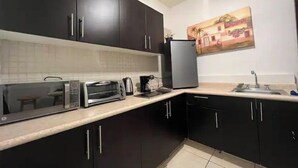 A kitchen with dark cabinets, a toaster, a coffee maker, and a refrigerator. - Apartament 2 beds+pool+gym+ petfriendly (Cabo San Lucas)