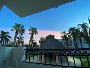 Un balcón con vistas a palmeras y un edificio con techo de paja.