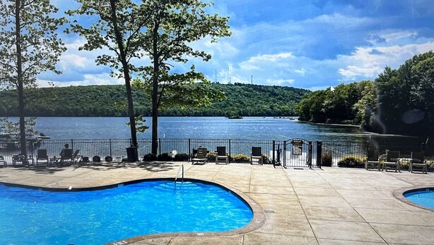 A swimming pool with lounge chairs and a view of a lake. - Beautiful, Cozy, All-Seasons Mountain/Lake Townhome (Lake Harmony)