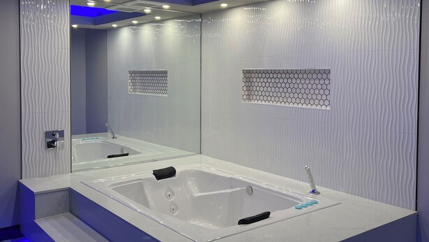 Casa de banho moderna com uma banheira grande, um espelho e um padrão de azulejos hexagonais nas paredes.