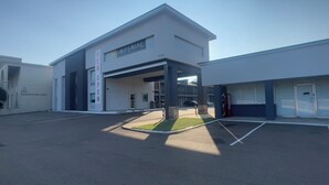 Entrada moderna de hotel com placa para Imperial Suites, área de estacionamento e máquina de refrigerantes Coca-Cola.