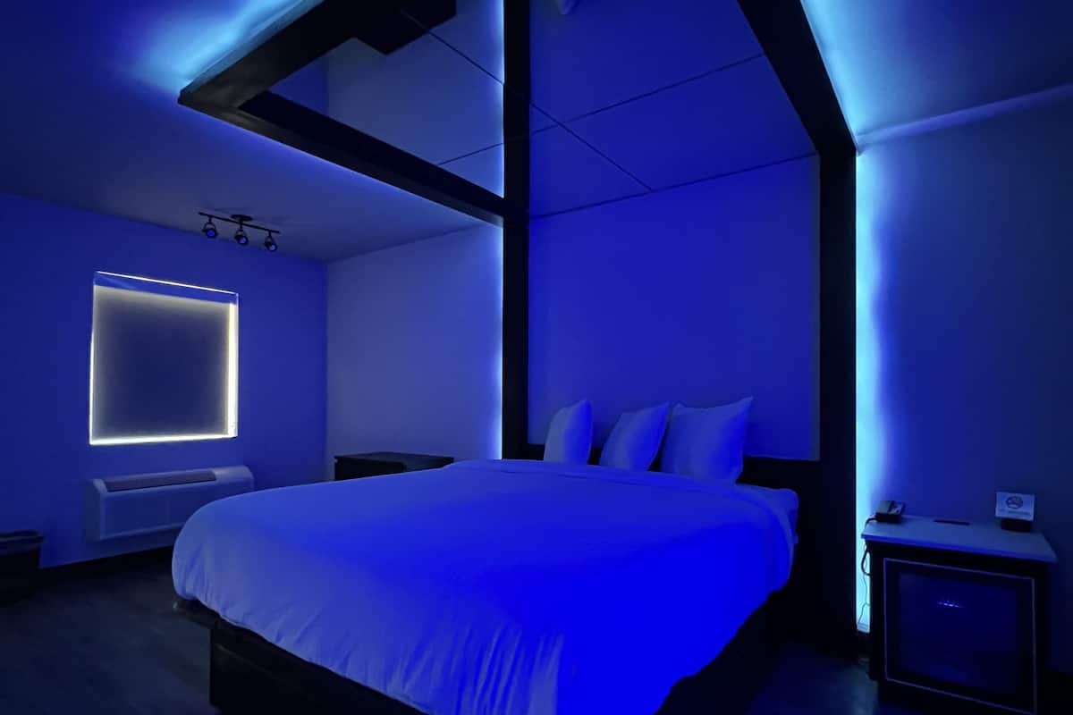 A modern bedroom with a large bed, a bedside table, a nightstand, and a wall-mounted light fixture.