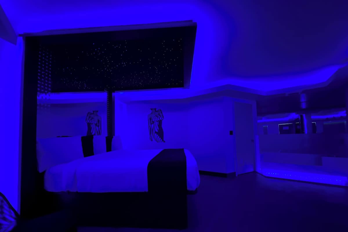 A modern bedroom with a large bed, a starry sky projection on the ceiling, and a minimalist design.