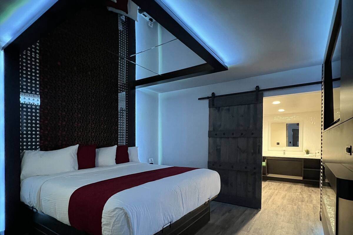 A modern bedroom with a bed, a dark headboard, and a wooden floor.
