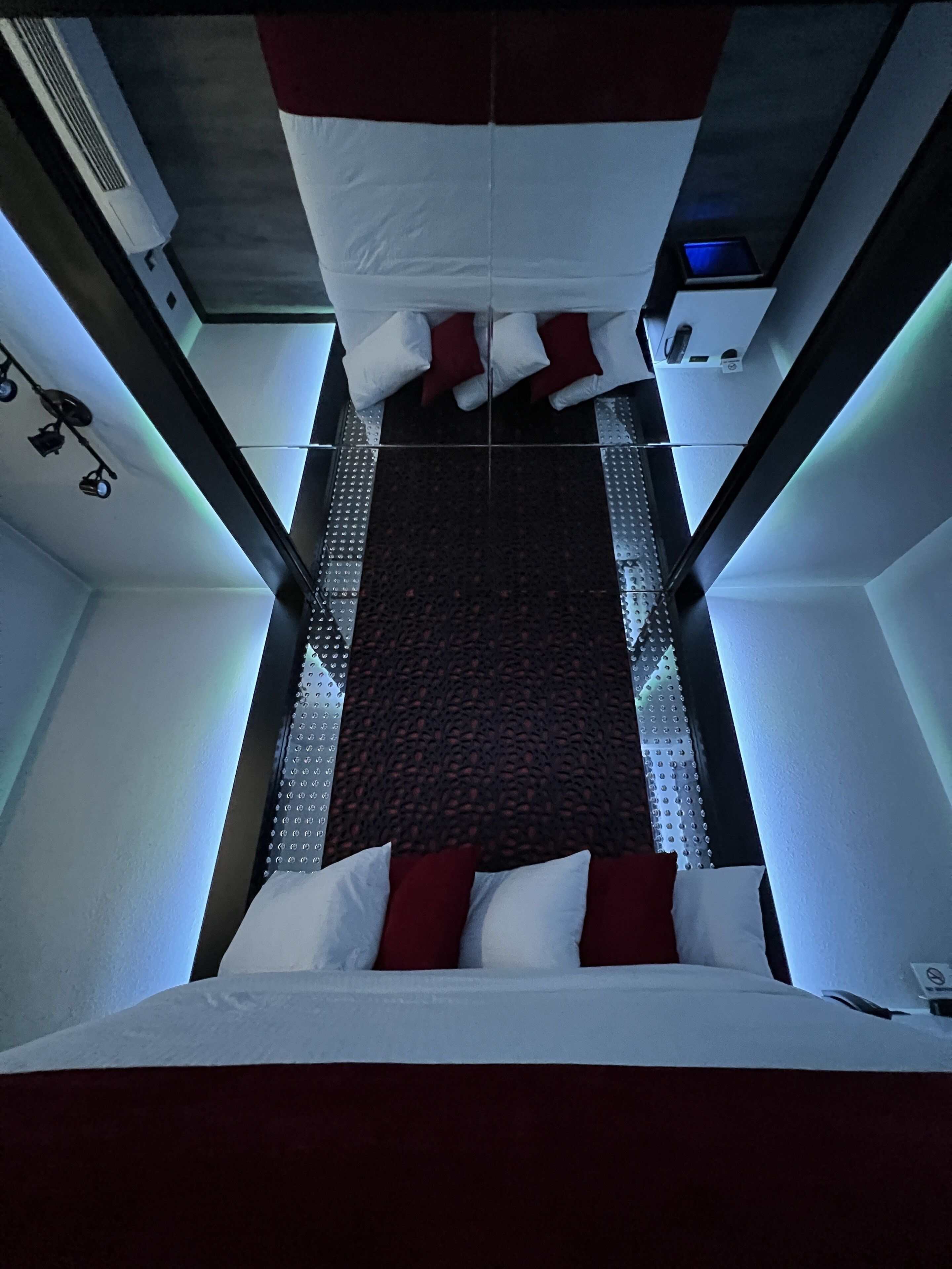 A modern hotel room with a bed, red and white bedding, a patterned carpet, and a ceiling with a ventilation system.