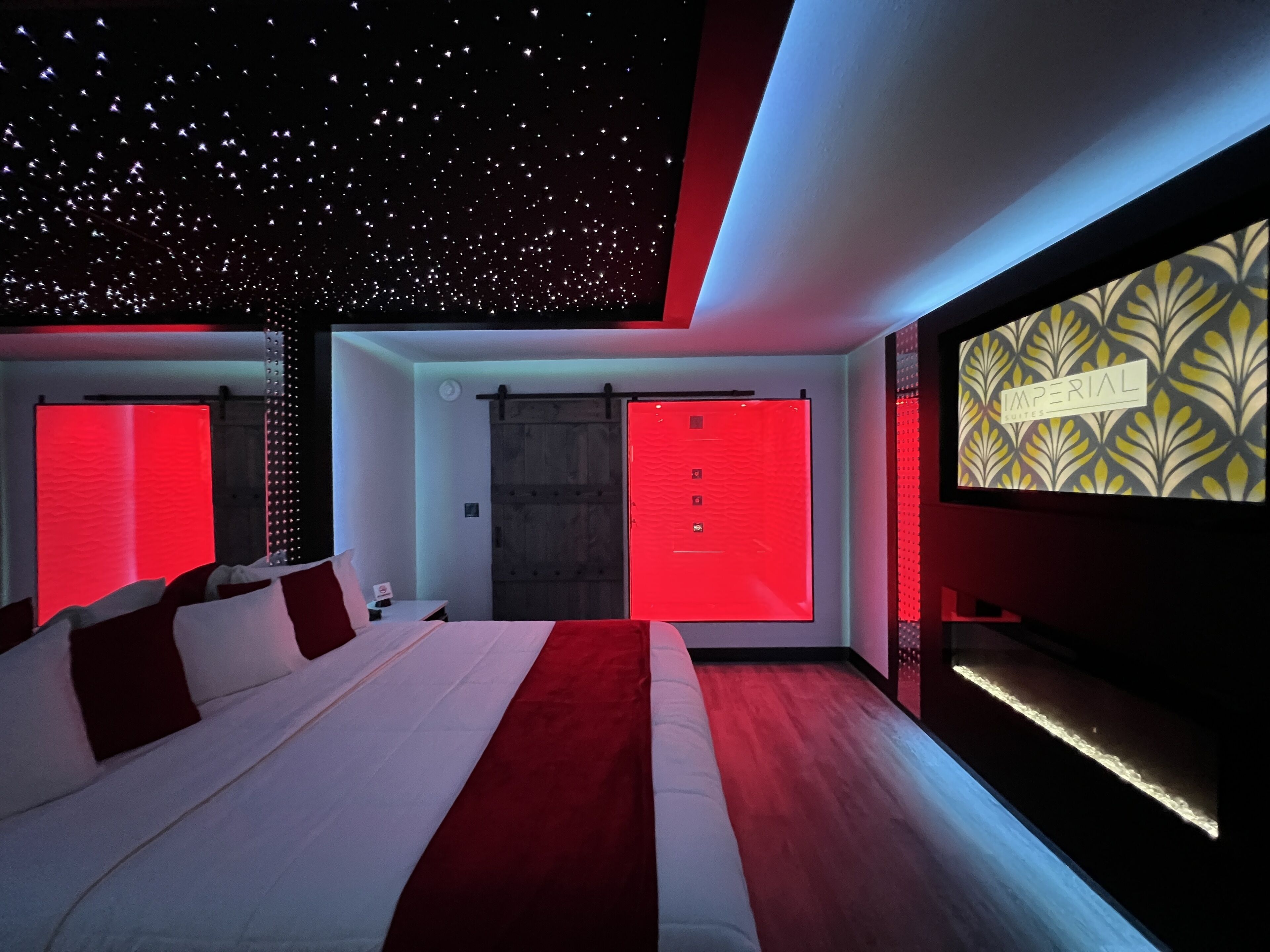 Una habitación de hotel moderna con una cama grande, un muro decorado en rojo y un diseño de techo que simula estrellas.