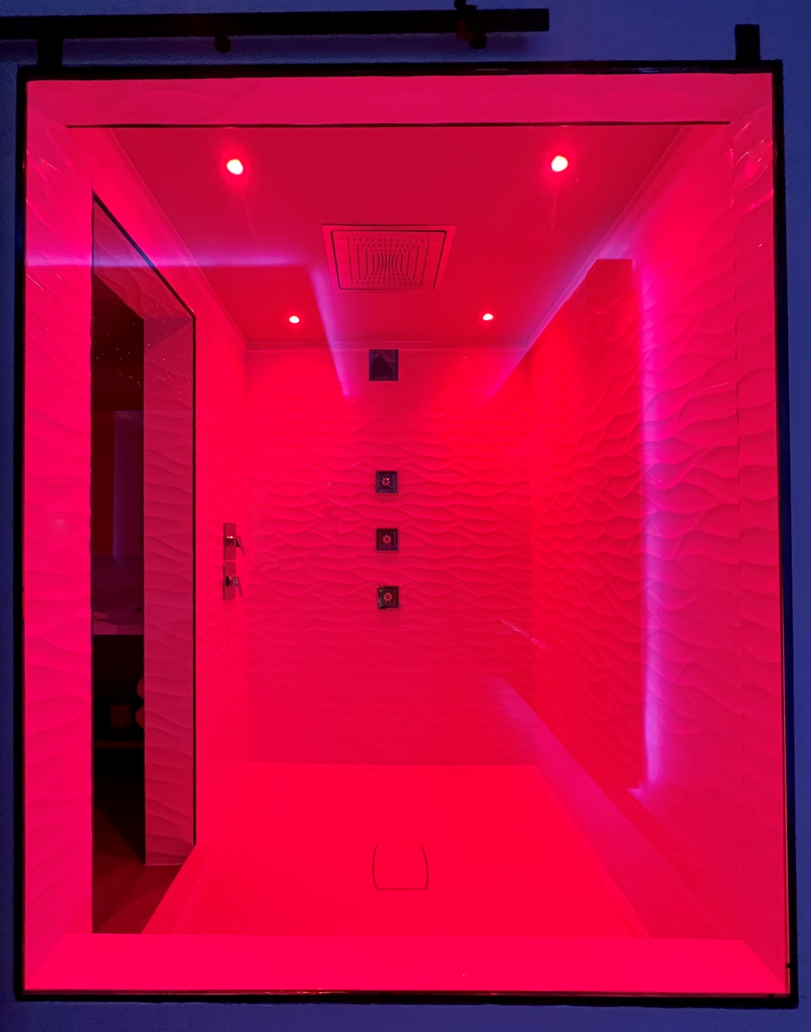 A red-lit room with a glass door, a textured wall, and a ceiling with recessed lighting.