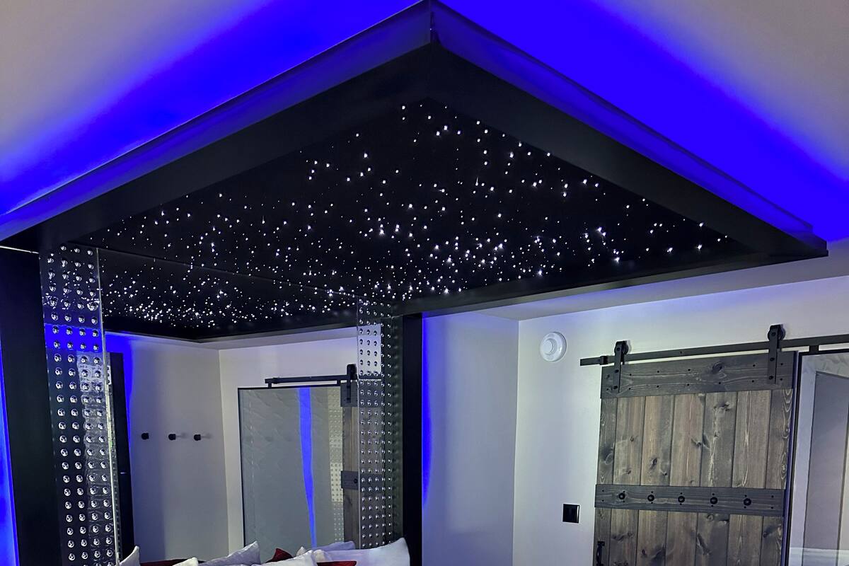 A modern bedroom with a large bed, a wooden wardrobe, and a starry ceiling design.