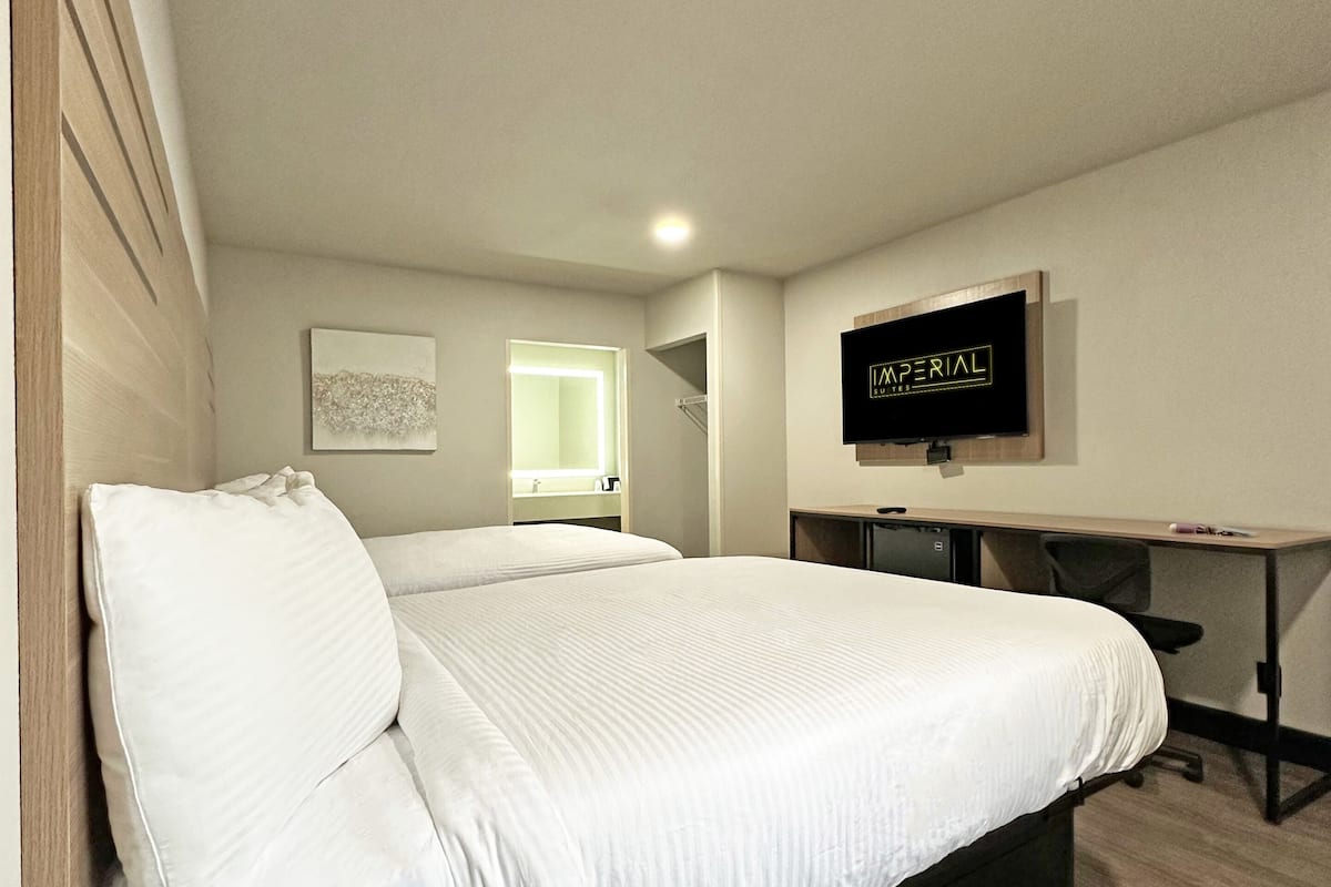 A bedroom with a bed, a desk, a chair, a TV, and a window.