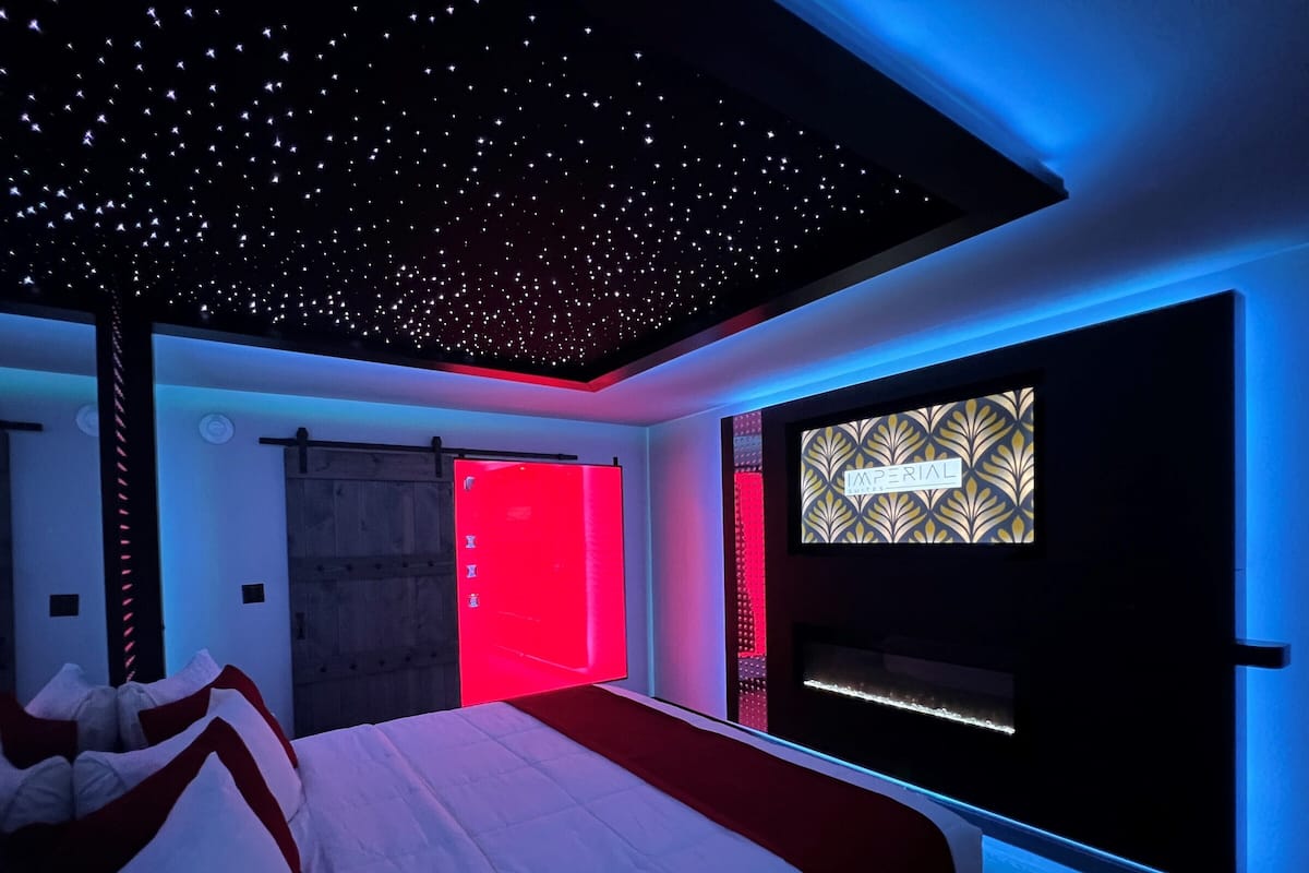 A modern bedroom with a bed, a red door, and a wall-mounted TV displaying 'IMPERIAL'.