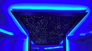 Quarto moderno com teto estrelado, cama curvada e iluminação azul ambiente.