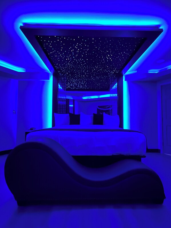 Un dormitorio moderno con techo estrellado, cama curvada e iluminación ambiental azul.