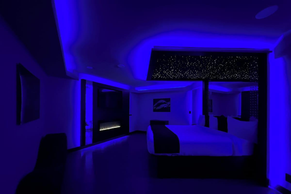 A modern bedroom with a bed, a desk, and a starry ceiling design.