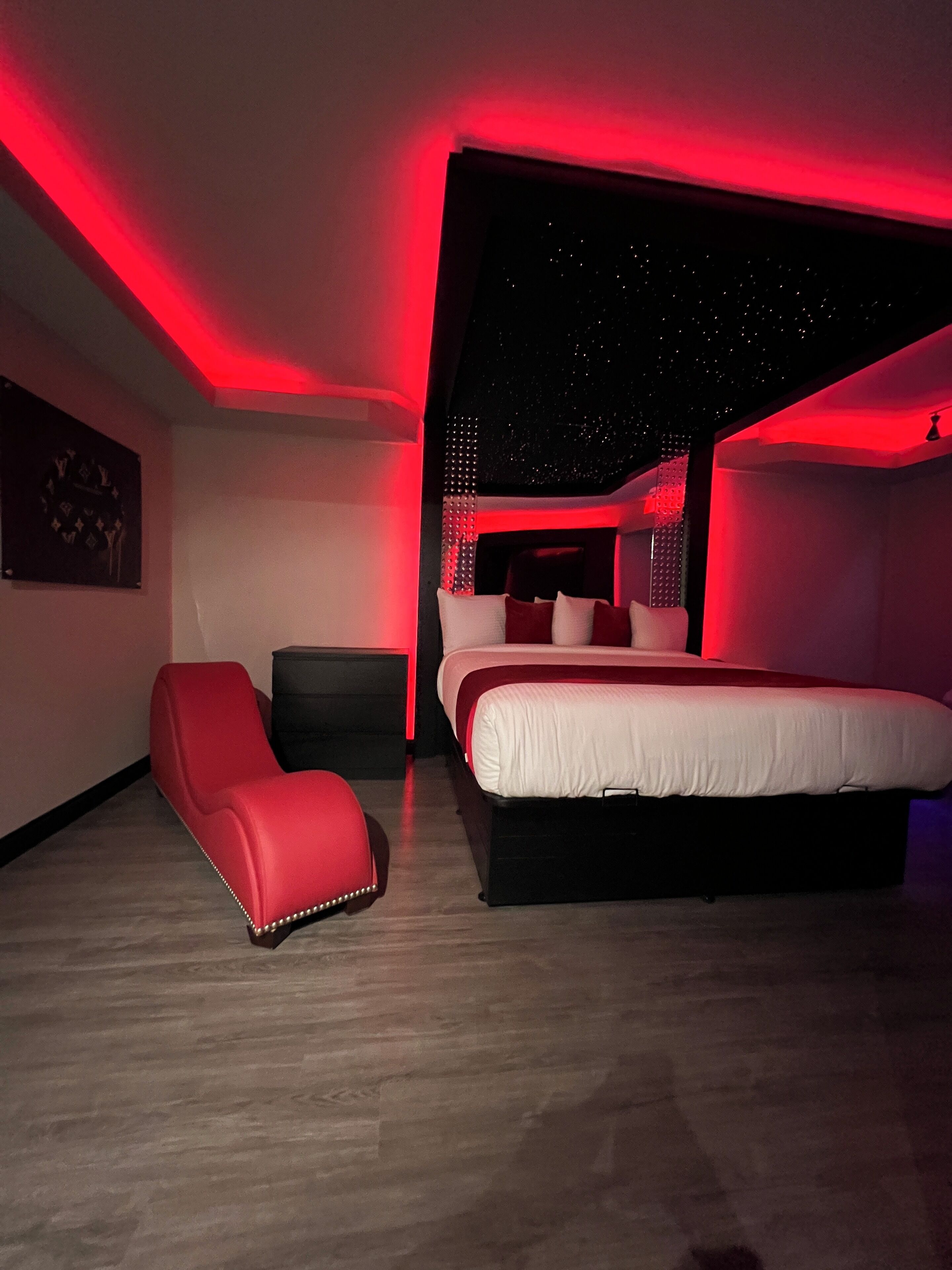 A modern bedroom with a large bed, a red chair, and a starry ceiling design.