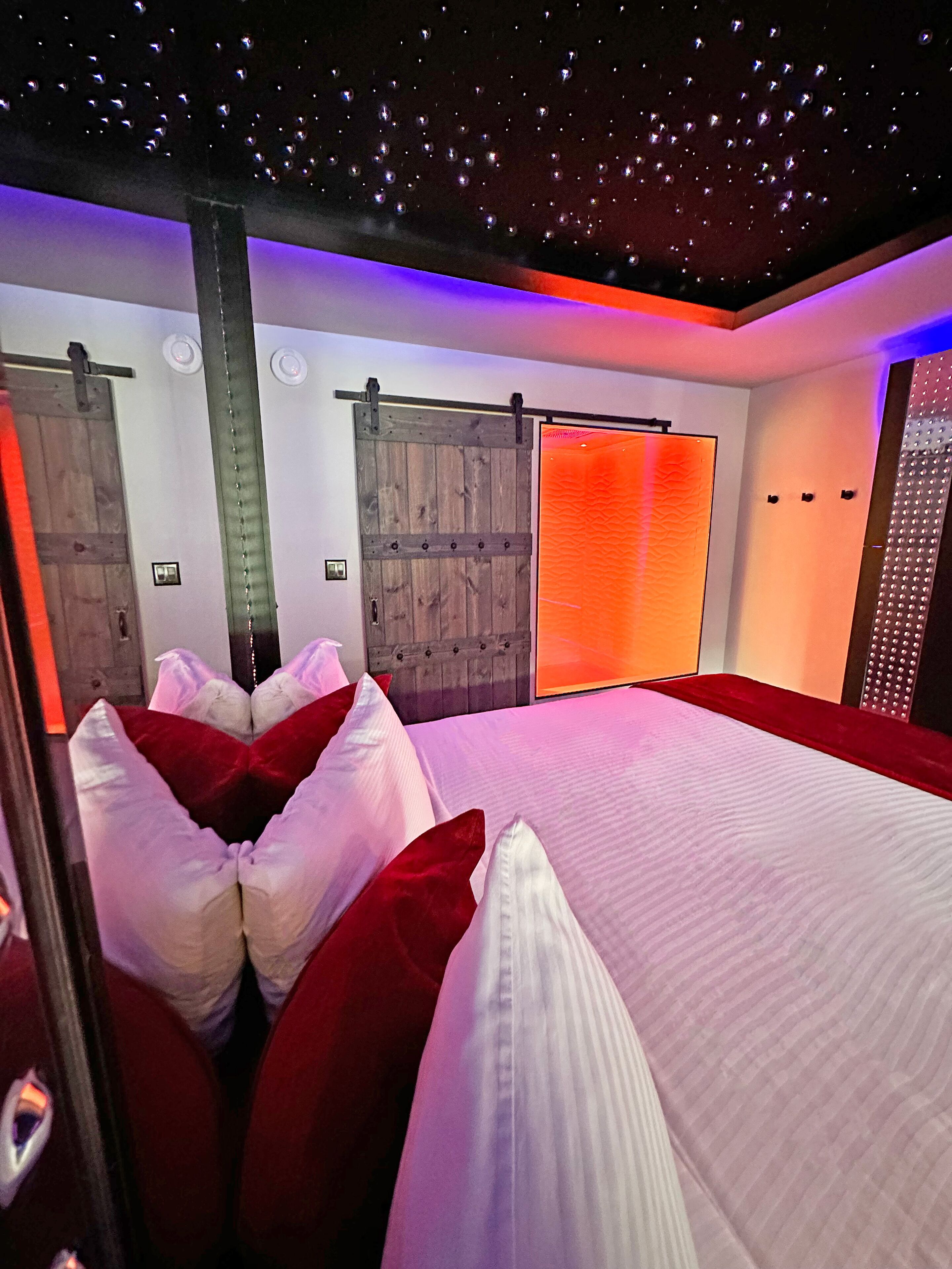 A bedroom with a starry ceiling, a wooden wardrobe, and a sliding door with an orange light.