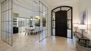 Un hall d’entrée spacieux comprenant un coin repas, une cloison en verre et une porte noire donnant sur l’extérieur.