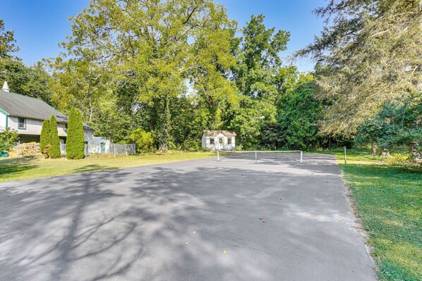 A tennis court with a net, surrounded by trees and a house in the background. - 3-Acre Property: Charming Dutch Country Colonial (Reading)