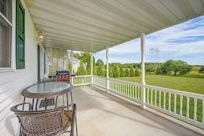 A covered porch with a table and chairs, a grill, and a view of a green landscape. - Charming Lewisburg Home w/ Hot Tub & Games! (Lewisburg)