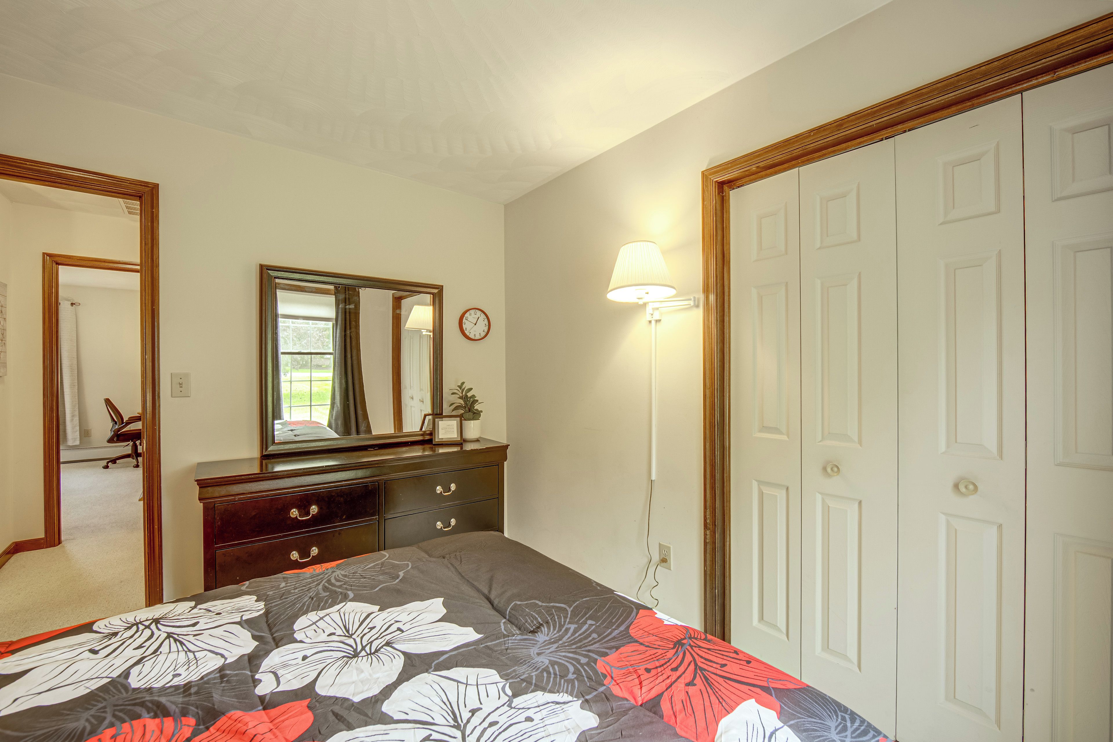 Un dormitorio con cama, cómoda, espejo, reloj de pared y una puerta.