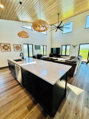 A modern kitchen with a large island, black cabinetry, and a farmhouse-style ceiling. - Modern Home with Private Big Horn River Access (Fort Smith)