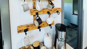 En vægmonteret kopholder med forskellige kopper og en kaffemaskine på en bordplade.