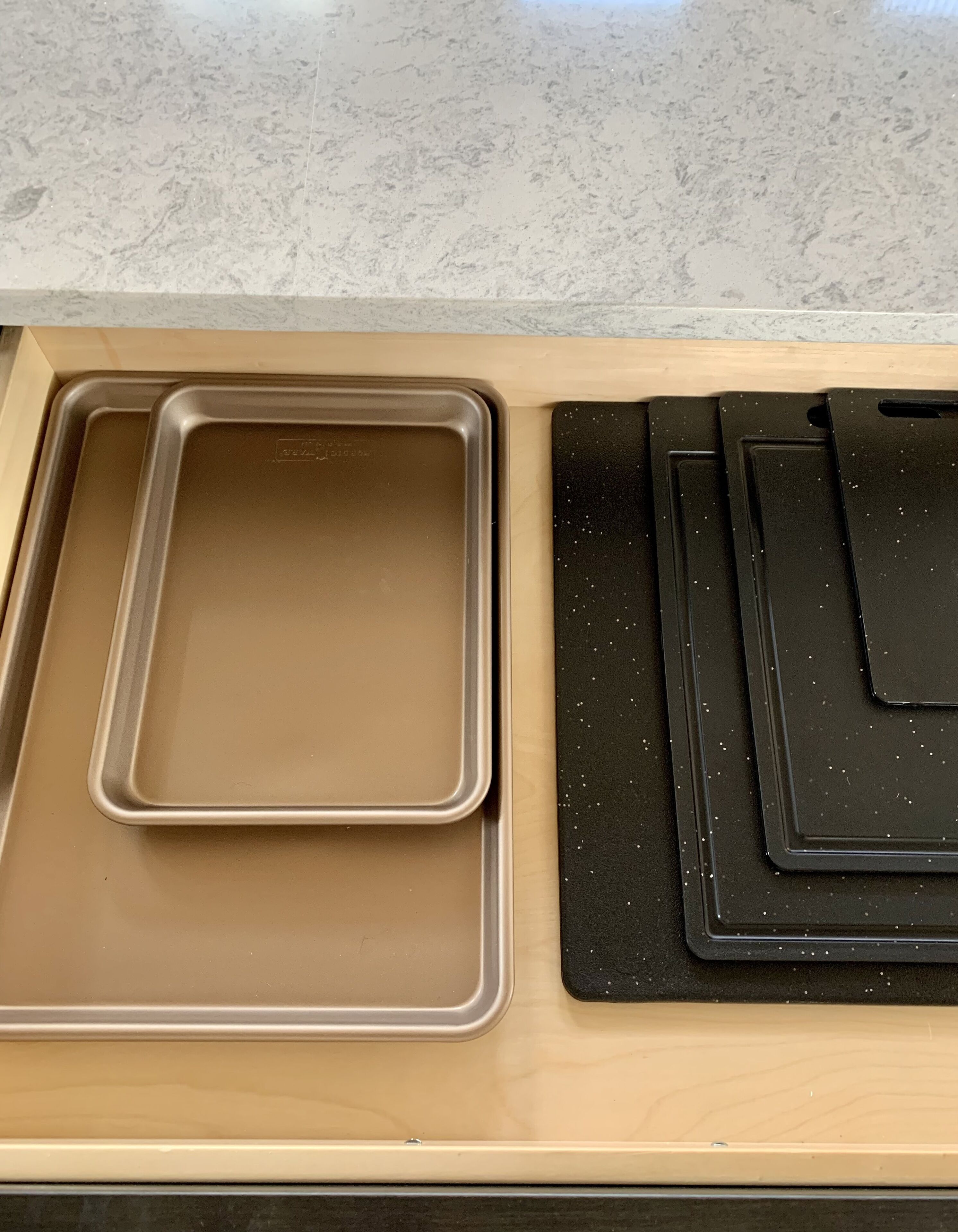 A kitchen drawer with a metal baking tray and a black cutting board.