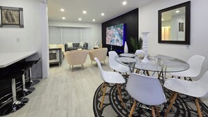 A modern living room with a dining area, a flat-screen TV, and a large mirror. - Ultimate Retreat: 98" Cinema + Arcade Game Room + BBQ + Airport (Brampton)