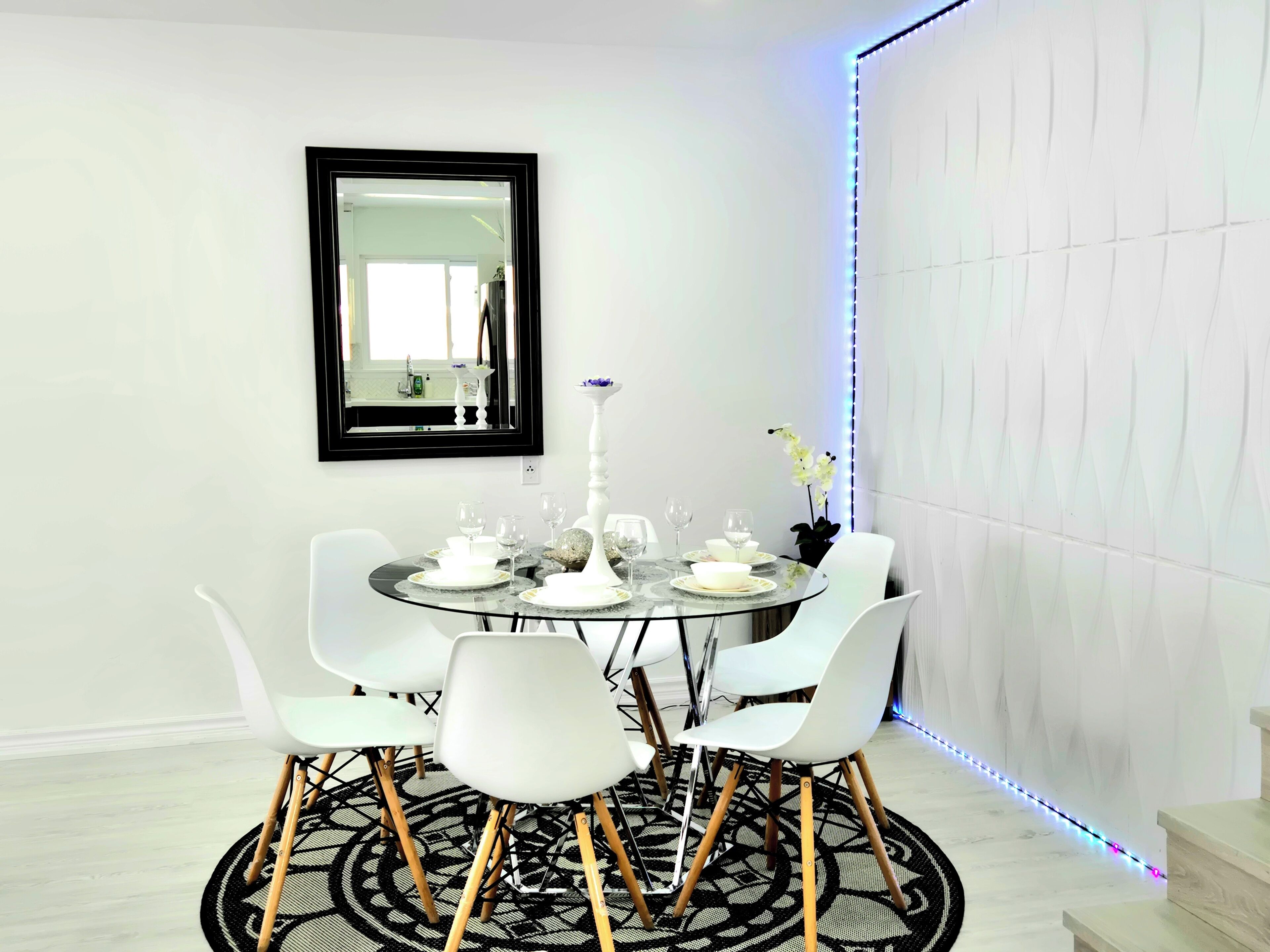 A dining area with a round table, white chairs, a mirror, and a decorative vase.