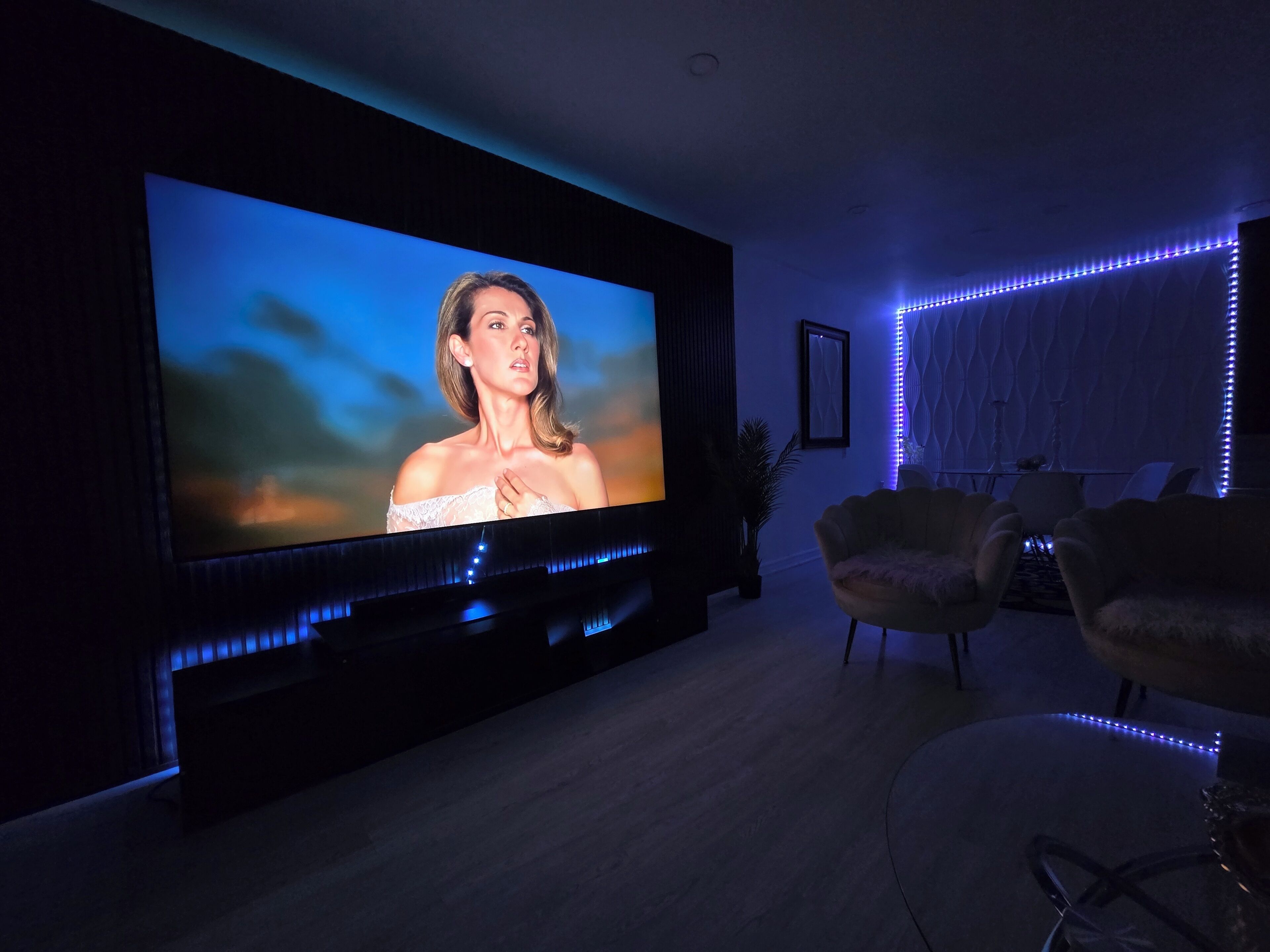 Una sala de estar moderna con un televisor de pantalla plana grande montado en la pared, un mueble de entretenimiento oscuro e iluminación LED azul ambiental.
