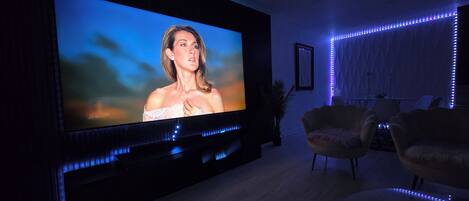 Una sala de estar moderna con un televisor de pantalla plana grande montado en la pared, un mueble de entretenimiento oscuro e iluminación LED azul ambiental.