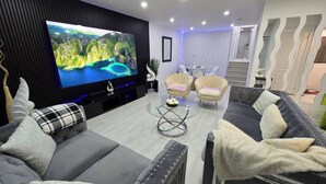 A modern living room with a large flat-screen TV, two armchairs, a sofa, and a glass coffee table. - Ultimate Retreat: 98" Cinema + Arcade Game Room + BBQ + Airport (Brampton)