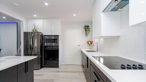A modern kitchen with stainless steel appliances, white cabinetry, and a light-colored floor. - Ultimate Retreat: 98" Cinema + Arcade Game Room + BBQ + Airport (Brampton)