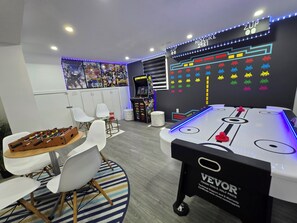 A room with a foosball table, a pool table, and a gaming machine.