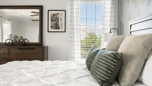 A bedroom with a bed, a dresser, a mirror, a framed picture, and a window with blinds. - Stylish Central Tucson Family-sized Home with Bikes to Ride (Tucson)