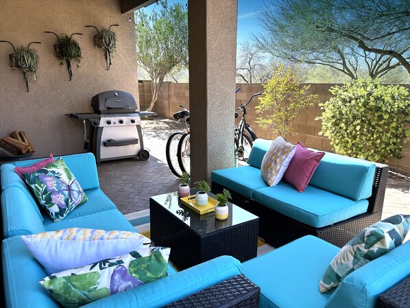 An outdoor seating area with a blue sofa, a small table with a plant, and a grill.