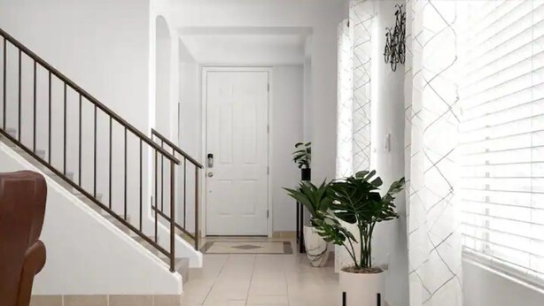 A hallway with a staircase, a white door at the end, and potted plants along the wall. - Stylish Central Tucson Family-sized Home with Bikes to Ride (Tucson)