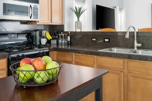 A kitchen with a microwave, stove, sink, and a fruit bowl on the counter.