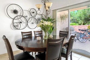 Uma área de refeições com uma mesa redonda, seis cadeiras, um vaso com flores e decorações de rodas de bicicleta fixadas na parede.