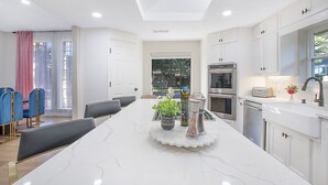 A modern kitchen with white cabinetry, a marble countertop, and a central island with seating. - ★4BR Dallas Family Estate | Heated Pool + Hot Tub | Sleeps 16 | Lake Highlands★ (Dallas)
