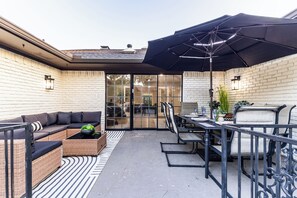 An outdoor patio with a black umbrella, wicker furniture, and a glass door leading to an interior space. - ★4BR Dallas Family Estate | Heated Pool + Hot Tub | Sleeps 16 | Lake Highlands★ (Dallas)