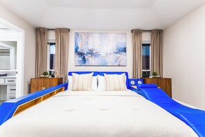 A modern bedroom with a large bed, a blue headboard, and a painting on the wall. - ★4BR Dallas Family Estate | Heated Pool + Hot Tub | Sleeps 16 | Lake Highlands★ (Dallas)