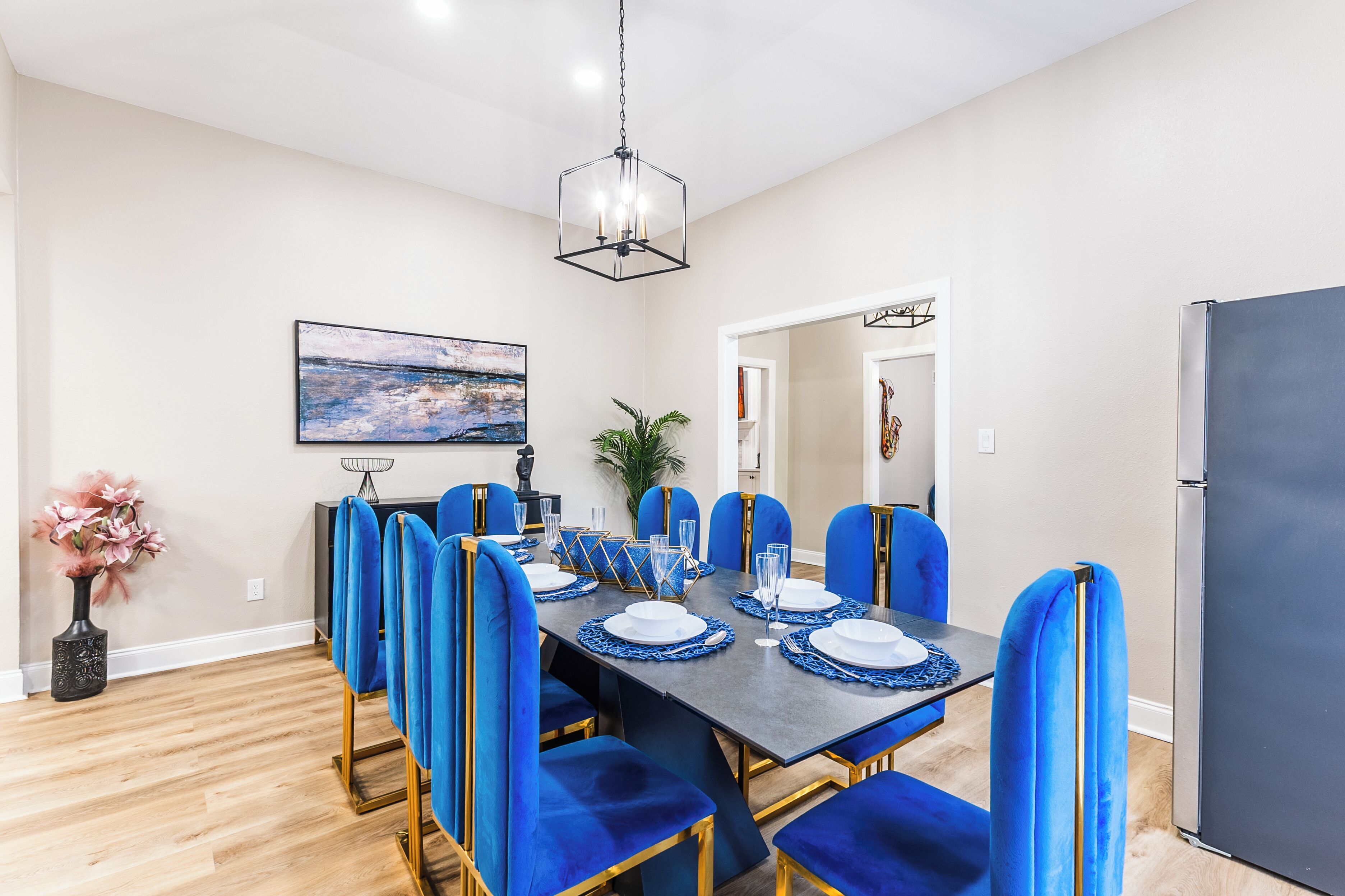A dining area with a rectangular table set for six, surrounded by six blue upholstered chairs with gold legs.