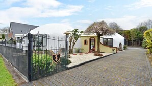 Zona residencial cerrada con un camino pavimentado que conduce a una casa de fachada blanca y techo de paja.