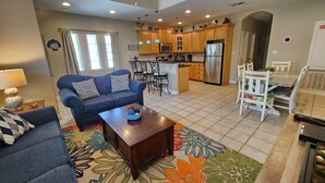 A spacious living area with a sofa, coffee table, and a kitchen in the background. - Cushy Crab, Pool and 3 Minute Walk to Beach!! (South Padre Island)