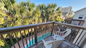 A wooden deck with two white plastic chairs, a pool, and palm trees in the background. - Cushy Crab, Pool and 3 Minute Walk to Beach!! (South Padre Island)