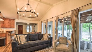 A spacious living room with a dark grey sofa, a patterned rug, and a large window with curtains. - Eatonton Getaway on Lake Sinclair w/ Dock! (Eatonton)